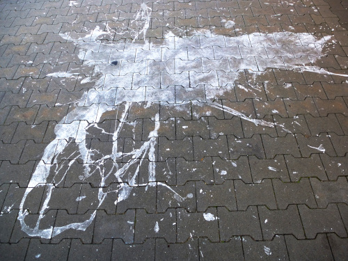 Der gepflasterte Boden des Bürgersteigs hat eine expressive Gestaltung erhalten, vermutlich durch einen verunglückten Eimer Wandfarbe.