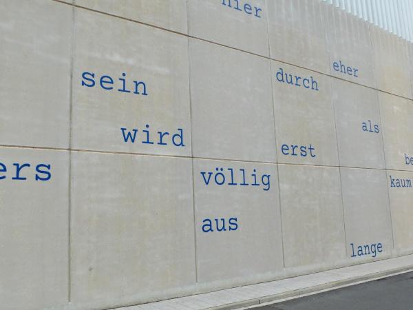 Auf grauer Betonwand stehen Wörter locker gestreut: sein, wird, völlig, aus, erst, durch, eher, als, lange, kaum.